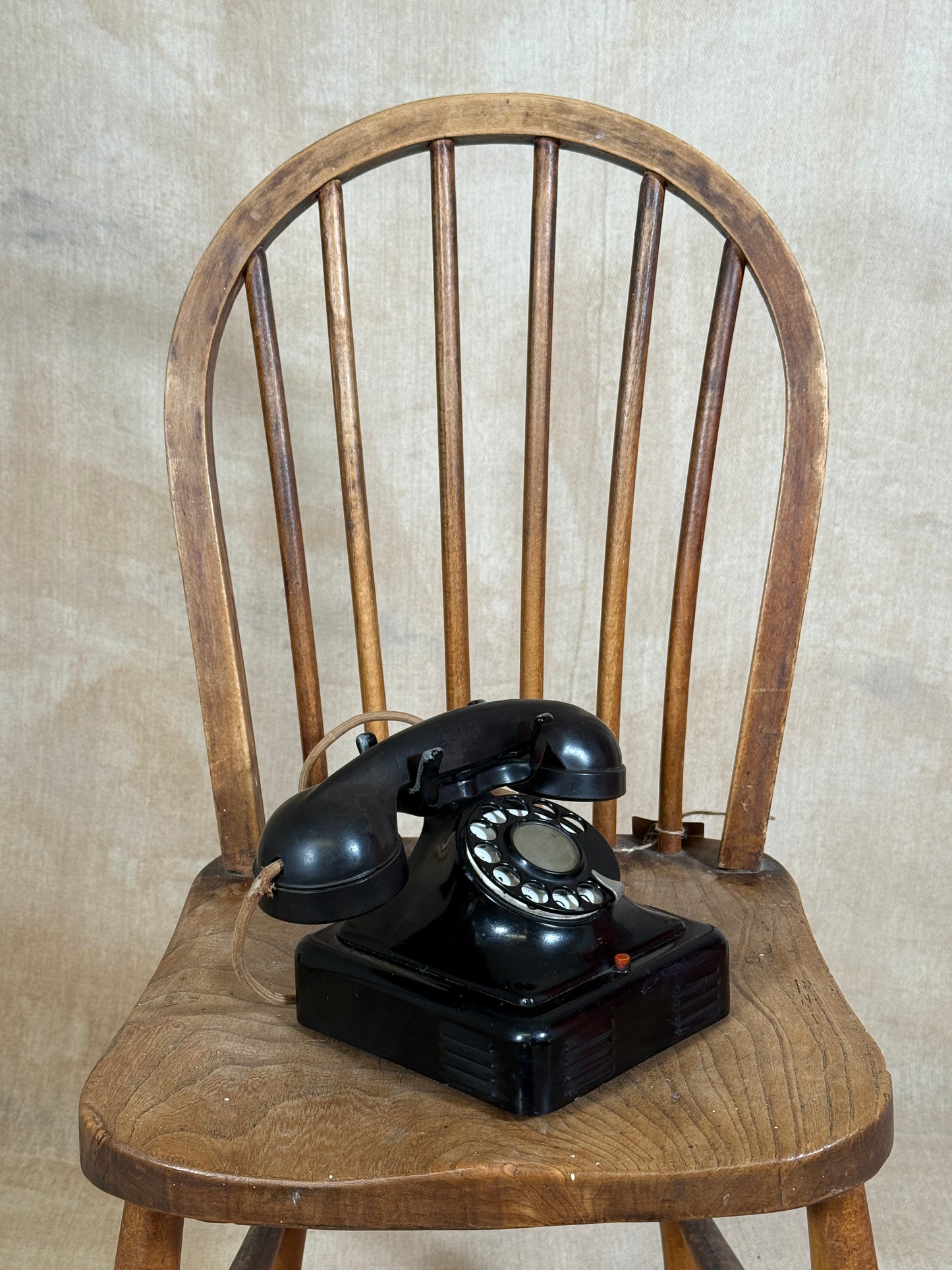 Vintage black rotary phone on a wooden chair with a neutral background