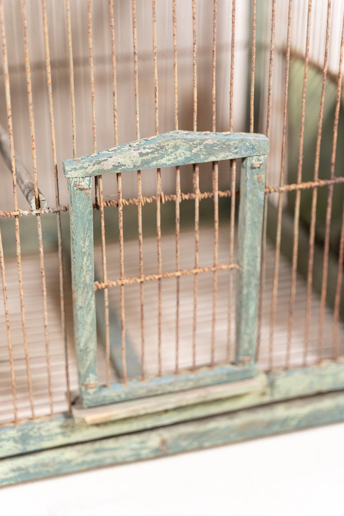 Vintage wooden birdcage with weathered green paint, decorative metal ridge detail, wire mesh panels and feeding troughs on both sides.