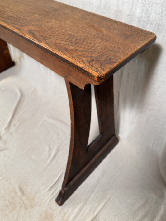 Traditional oak organ bench in the Gothic style, with a wide wooden seat and angled side frames.