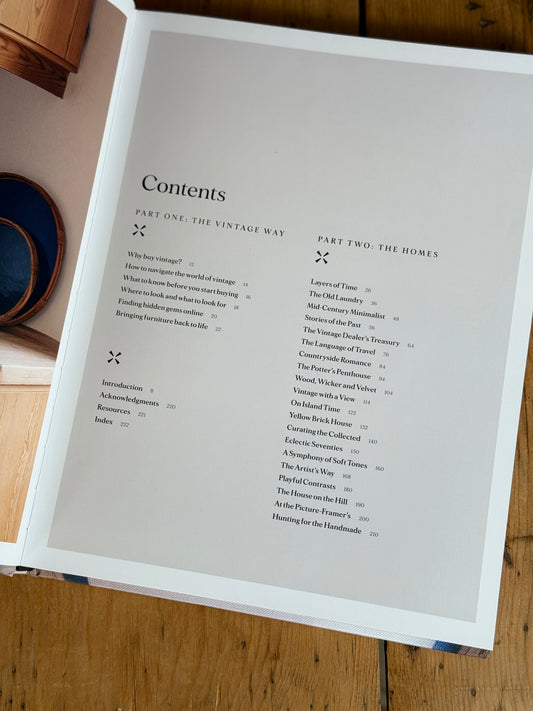 An open book showing a printed Contents page with text columns on white paper, photographed on a wooden tabletop with part of a blue bowl visible at the left edge.