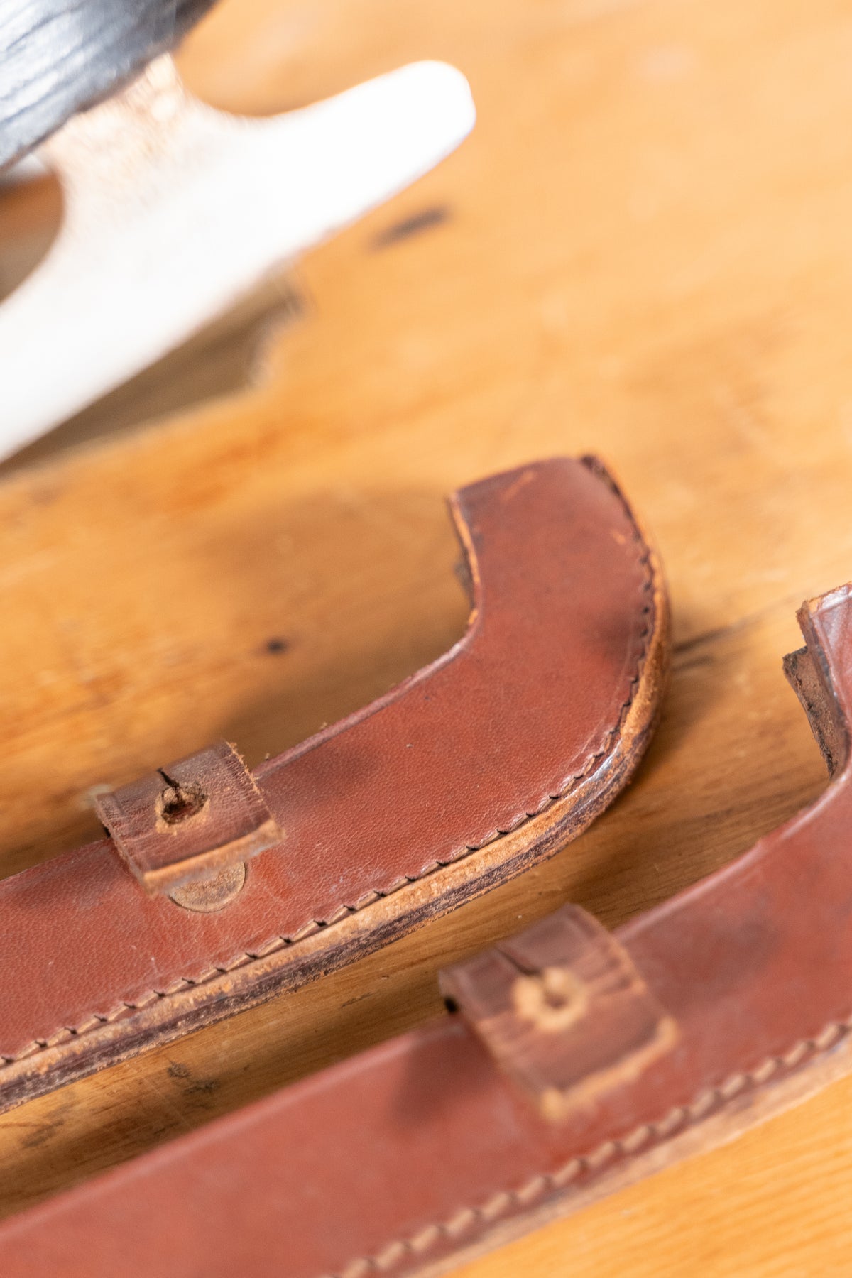 Close-up of two brown leather straps with stitched edges and small metal rivets, laid on a wooden surface.