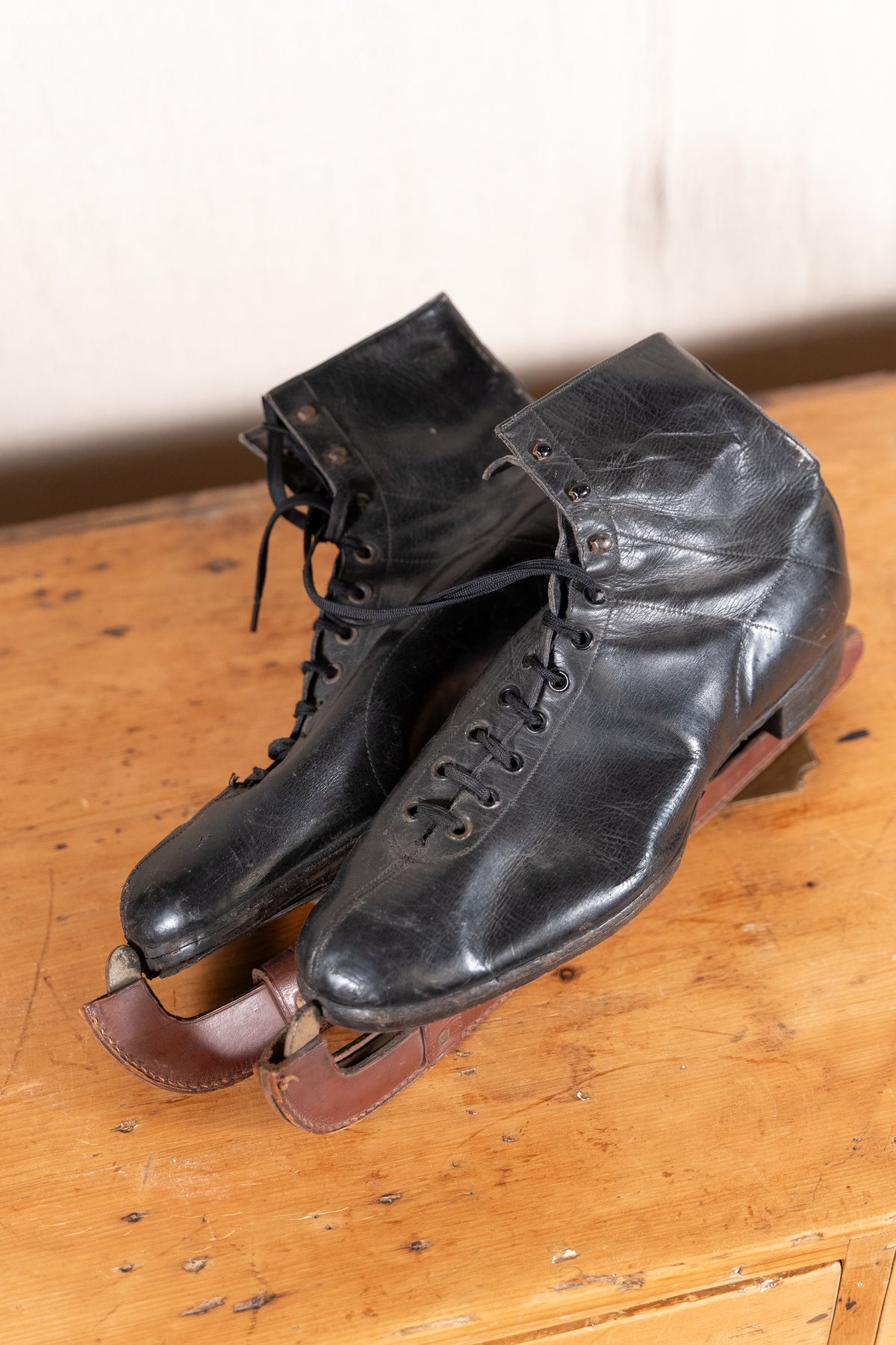 A pair of vintage black leather ice skates with brown leather straps and metal blades, resting on a rustic wooden table.