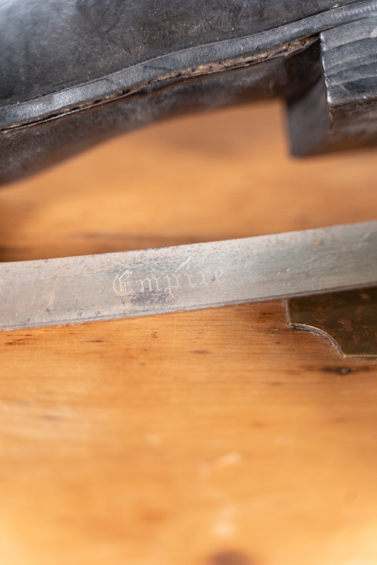 Close-up of a metal ice scate blade with engraved 'Empire' resting on a warm wooden surface, with part of a black leather boot visible at the top.