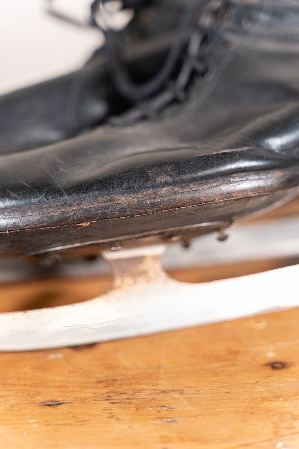 A close-up of a worn black leather ice skate boot with a metal blade resting on a wooden surface.