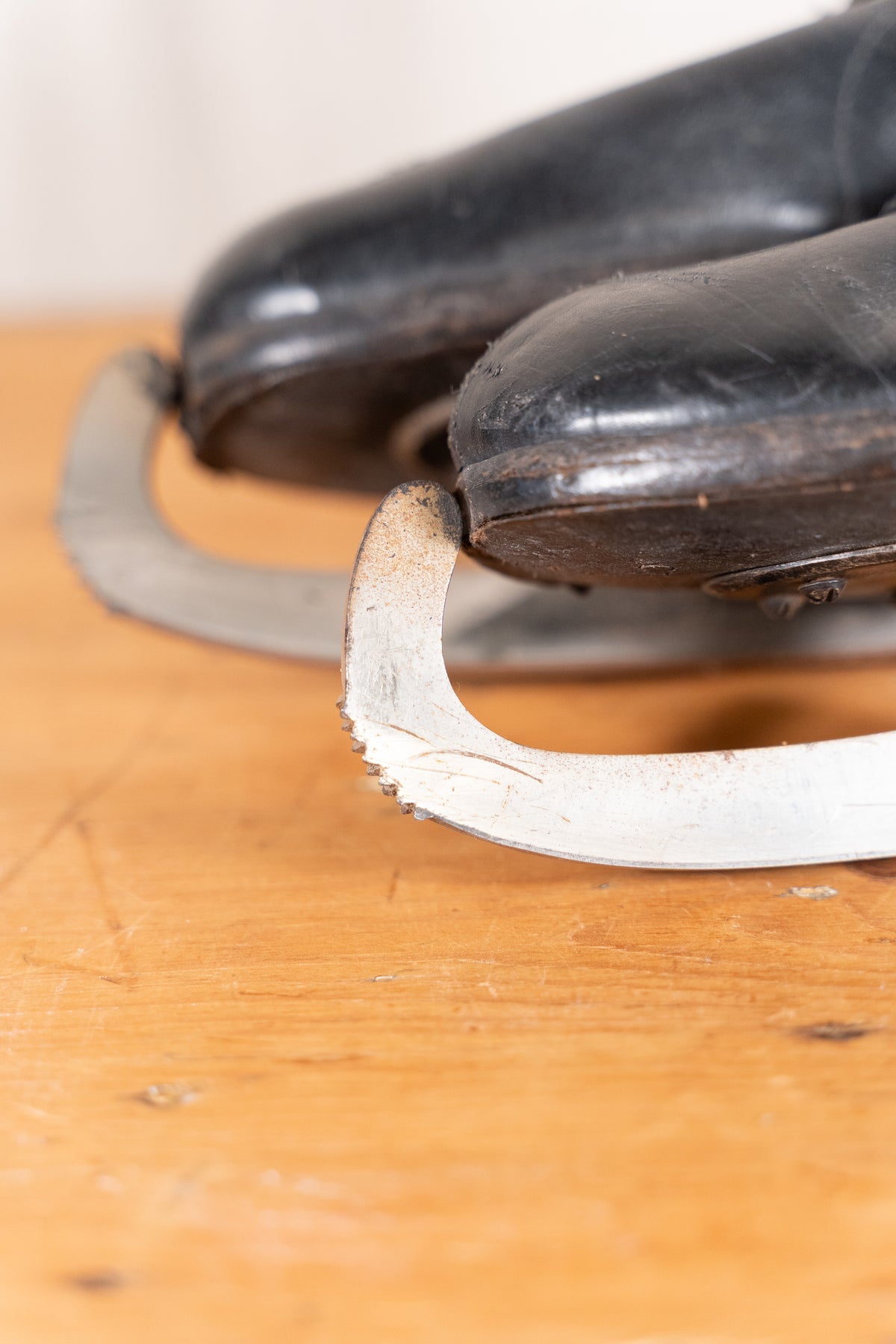 A close-up shot of a pair of vintage black ice skates resting on a wooden surface, highlighting the worn metal blades.