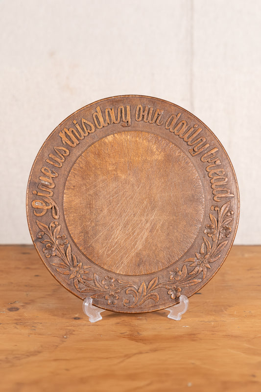 Vintage wooden bread board carved with “Give Us This Day Our Daily Bread” and a decorative floral and wheat motif around the rim.