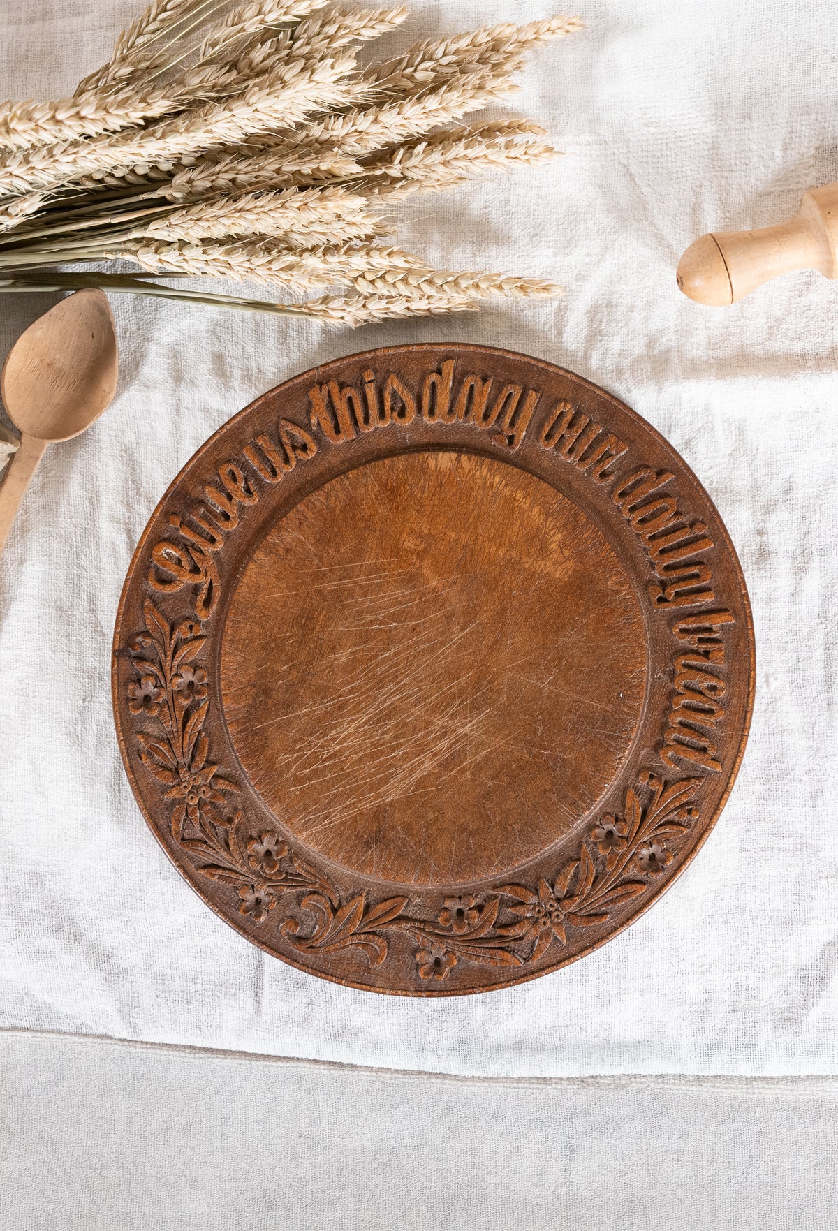 Vintage wooden bread board carved with “Give Us This Day Our Daily Bread” and a decorative floral and wheat motif around the rim.