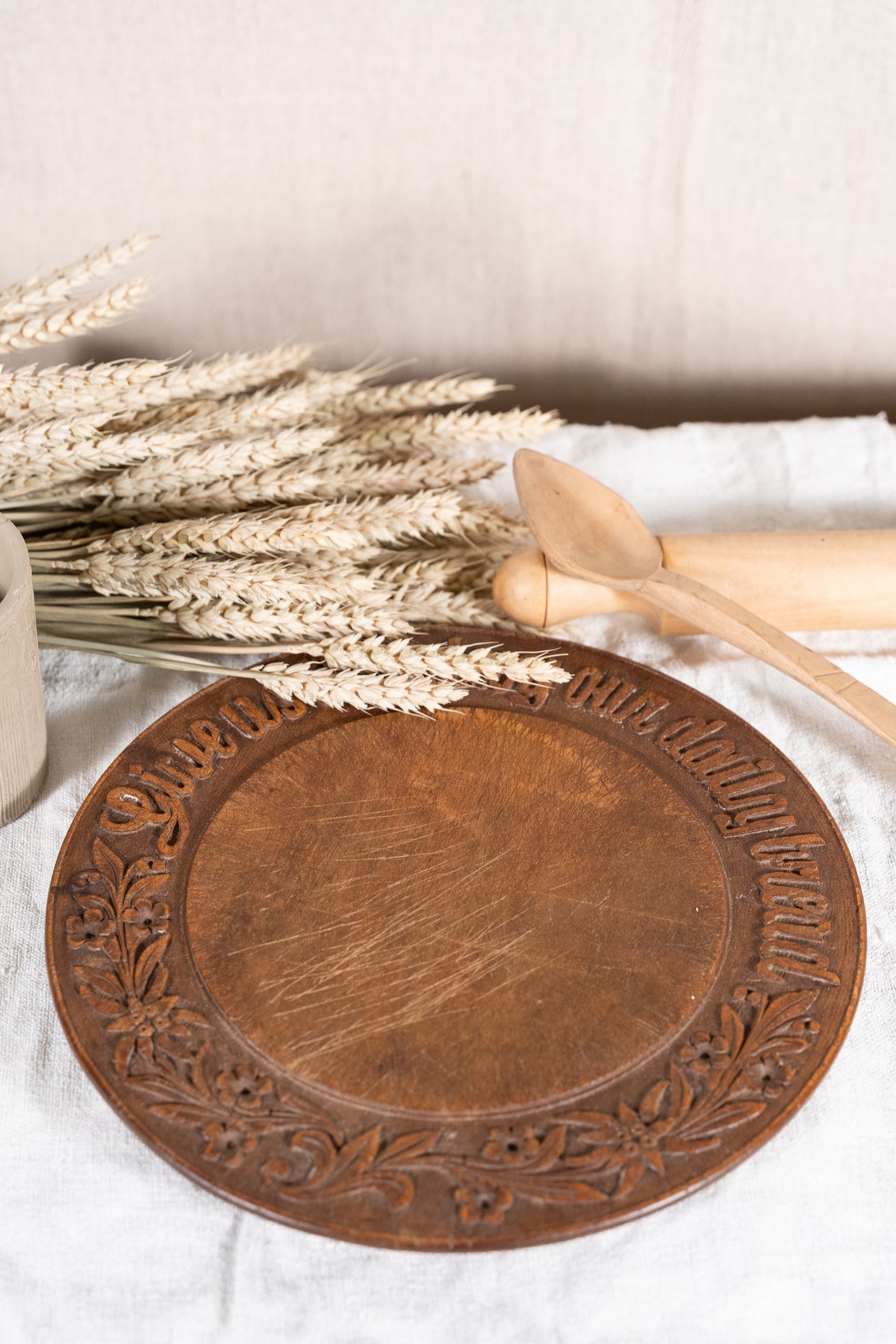 Vintage wooden bread board carved with “Give Us This Day Our Daily Bread” and a decorative floral and wheat motif around the rim.