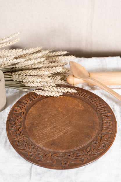 Vintage wooden bread board carved with “Give Us This Day Our Daily Bread” and a decorative floral and wheat motif around the rim.