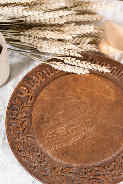 Vintage wooden bread board carved with “Give Us This Day Our Daily Bread” and a decorative floral and wheat motif around the rim.