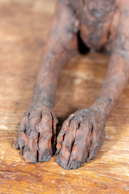 Close-up of a dark brown textured sculpture or figurine showing detailed paws and legs resting on a rustic wooden surface.