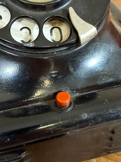 Close-up of a vintage phone with a rotary dial and an orange button.