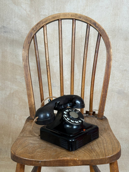 Vintage black rotary phone on a wooden chair with a neutral background