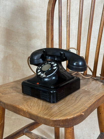 Vintage black rotary phone on a wooden surface with a beige background