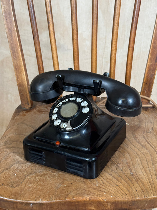 Vintage black rotary phone mounted on a wooden wall.