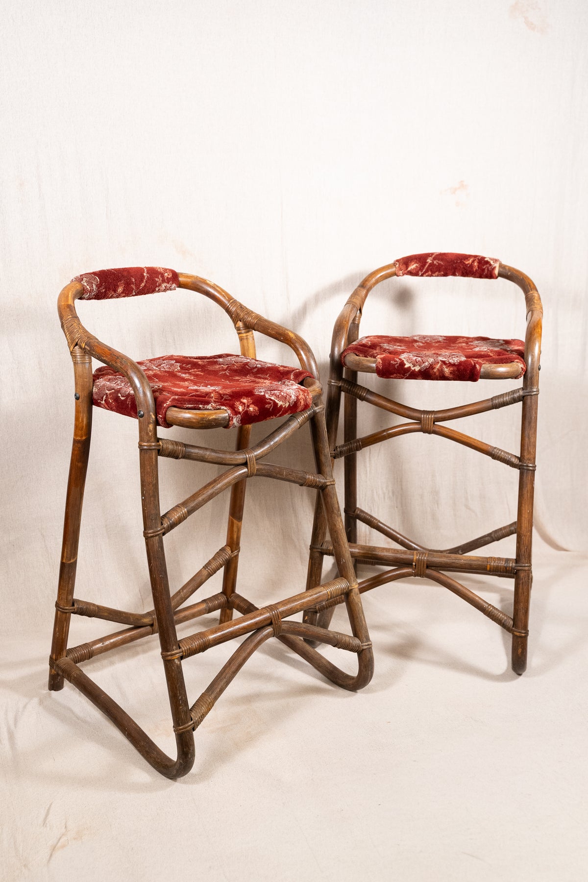 Pair of vintage bamboo bar stools with dark finished frames, red patterned velvet-style upholstery, X-shaped cross supports and lower footrests.