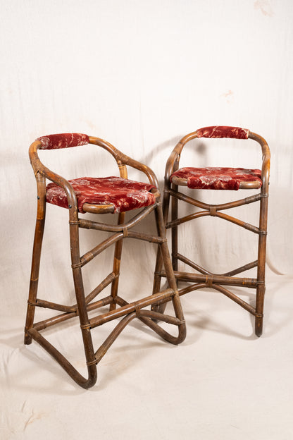 Pair of vintage bamboo bar stools with dark finished frames, red patterned velvet-style upholstery, X-shaped cross supports and lower footrests.
