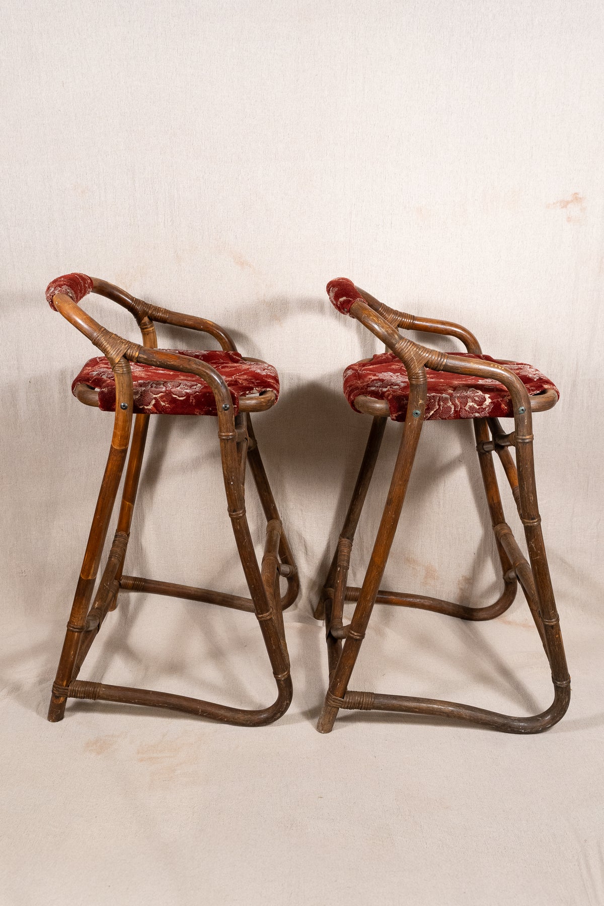 Pair of vintage bamboo bar stools with dark finished frames, red patterned velvet-style upholstery, X-shaped cross supports and lower footrests.