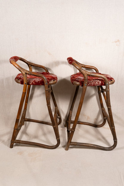 Pair of vintage bamboo bar stools with dark finished frames, red patterned velvet-style upholstery, X-shaped cross supports and lower footrests.