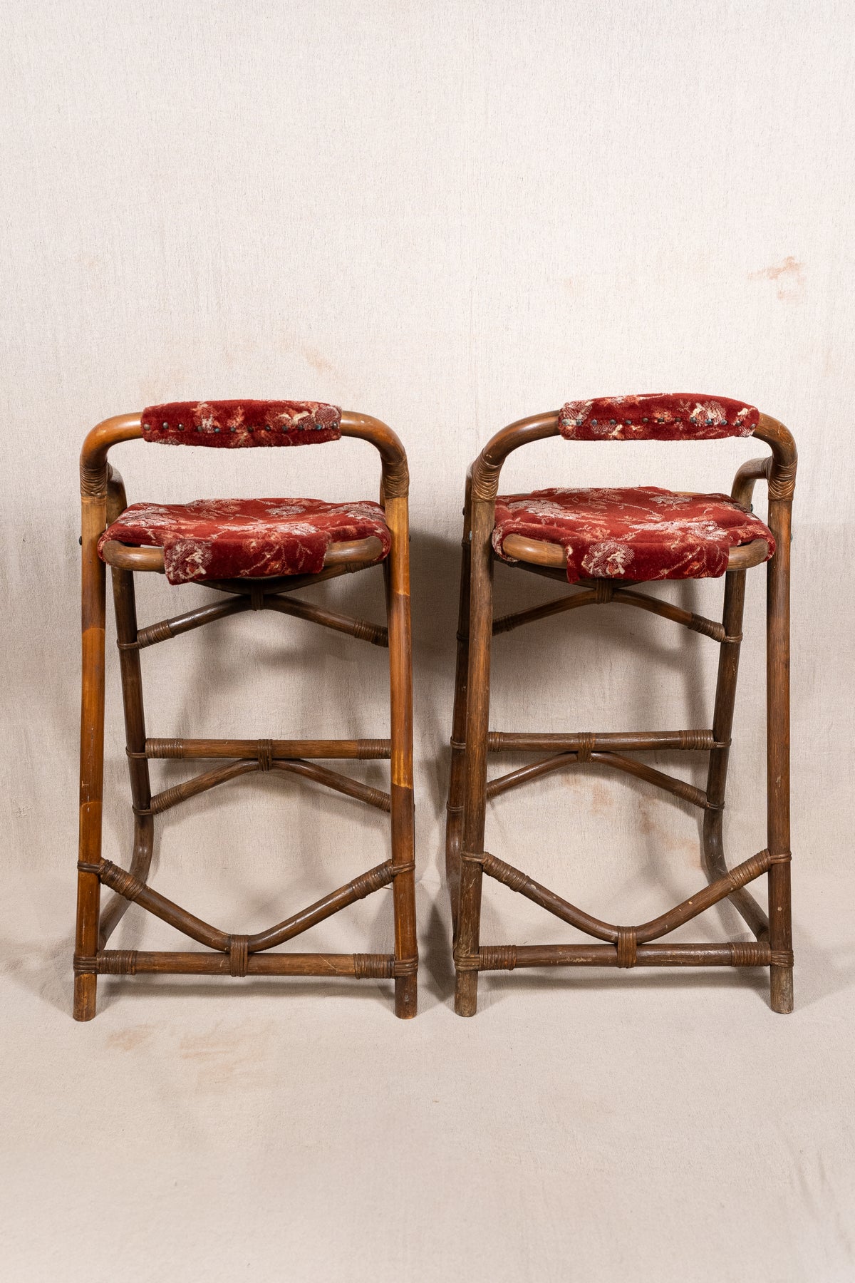 Pair of vintage bamboo bar stools with dark finished frames, red patterned velvet-style upholstery, X-shaped cross supports and lower footrests.