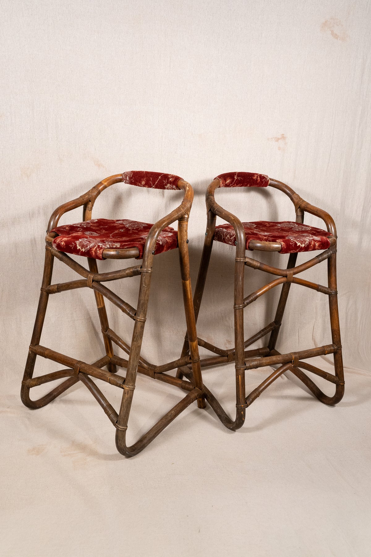 Pair of vintage bamboo bar stools with dark finished frames, red patterned velvet-style upholstery, X-shaped cross supports and lower footrests.
