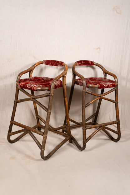 Pair of vintage bamboo bar stools with dark finished frames, red patterned velvet-style upholstery, X-shaped cross supports and lower footrests.