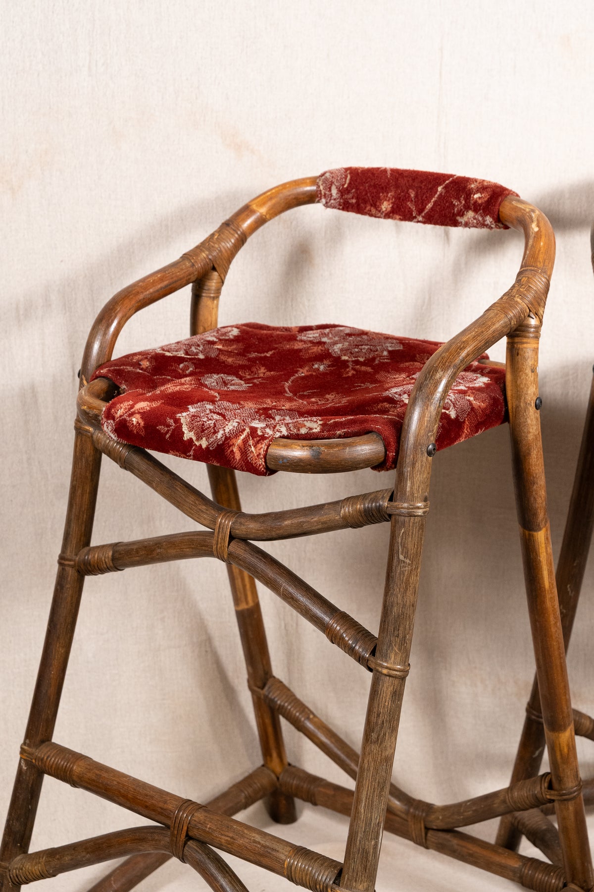 Pair of vintage bamboo bar stools with dark finished frames, red patterned velvet-style upholstery, X-shaped cross supports and lower footrests.
