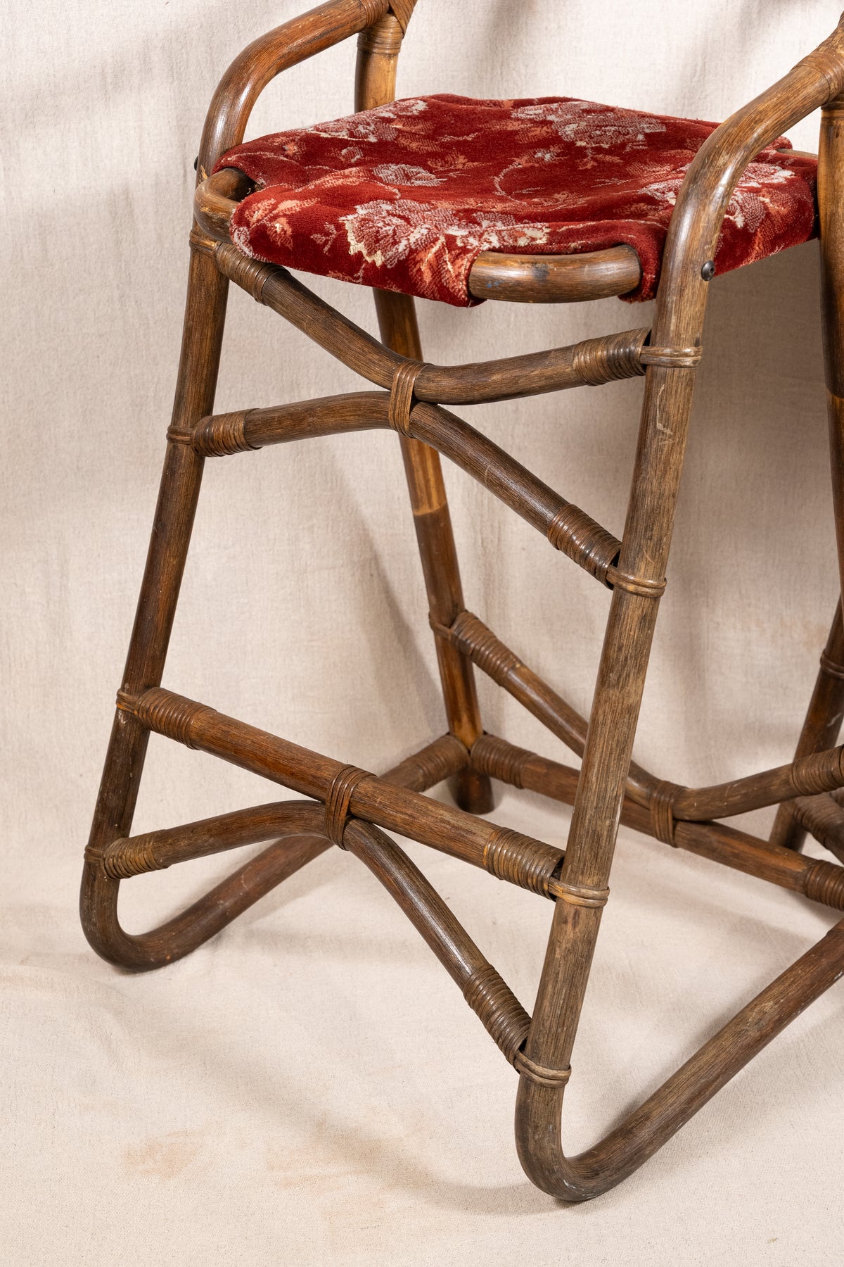 Pair of vintage bamboo bar stools with dark finished frames, red patterned velvet-style upholstery, X-shaped cross supports and lower footrests.