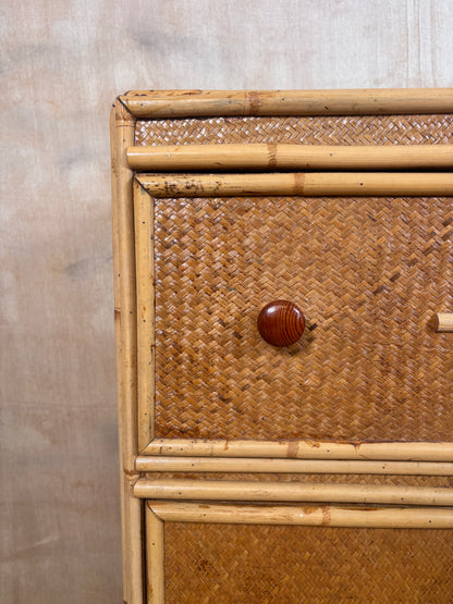 Close-up of a rattan and bamboo chest or cabinet drawer, showing woven natural-fiber panels, a round wooden knob, and light bamboo framing against a neutral textured wall.