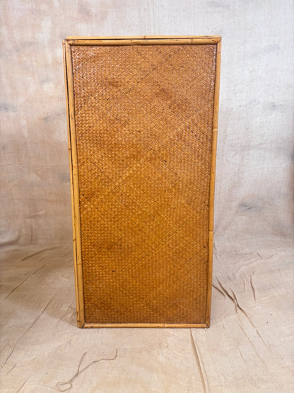 A rectangular vintage rattan or woven cane panel with a natural bamboo frame, standing upright against a neutral beige fabric backdrop.