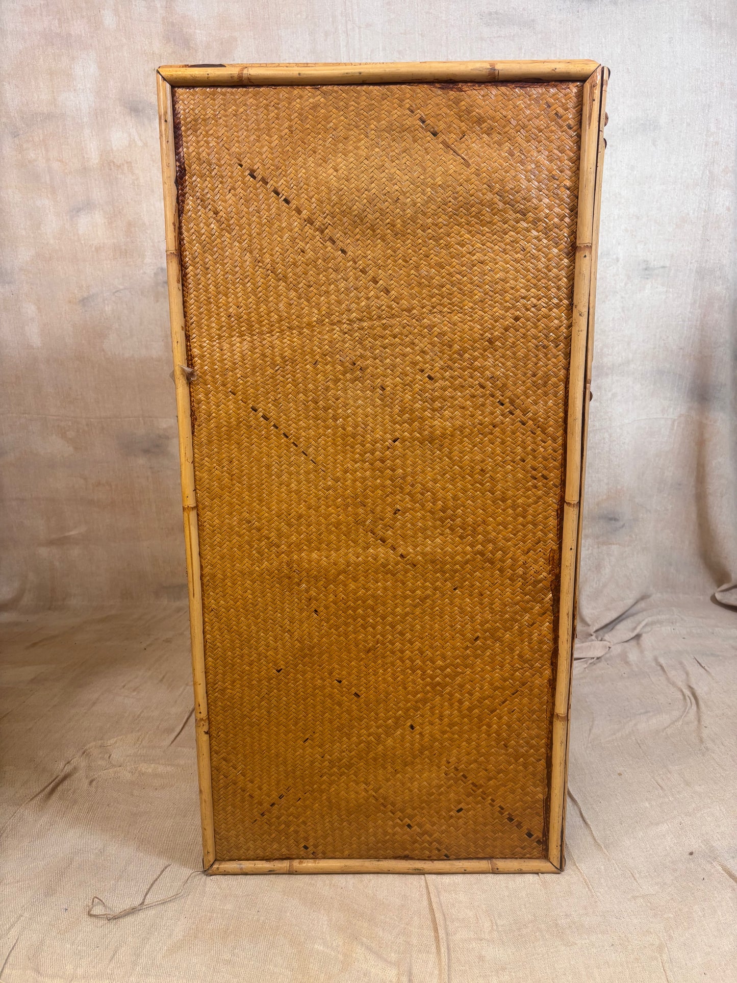 A rectangular bamboo frame with a tightly woven natural rattan or wicker panel, standing upright against a neutral fabric backdrop.