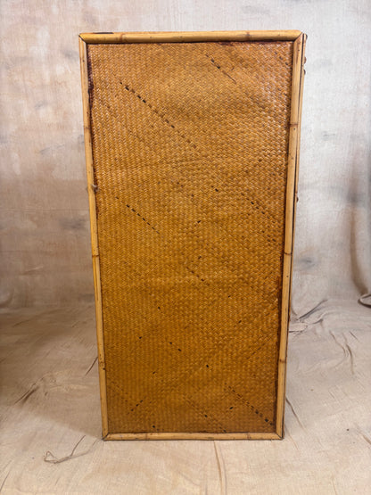 A rectangular bamboo frame with a tightly woven natural rattan or wicker panel, standing upright against a neutral fabric backdrop.