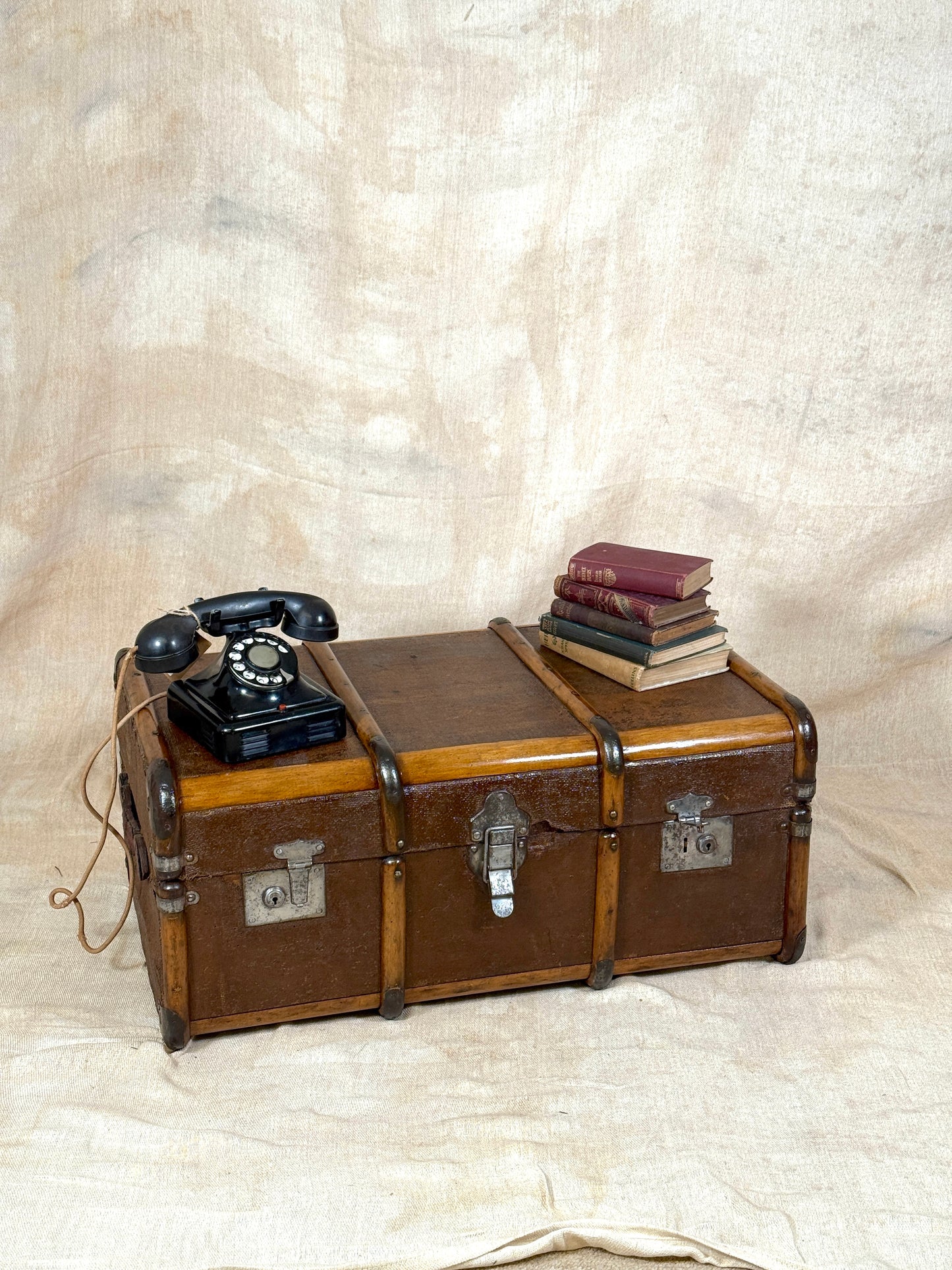 Vintage-style brown trunk with a black rotary phone and books on a textured beige background