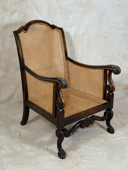 Antique Bergère style cane armchair and matching footstool with dark carved wooden frames and woven cane panels.