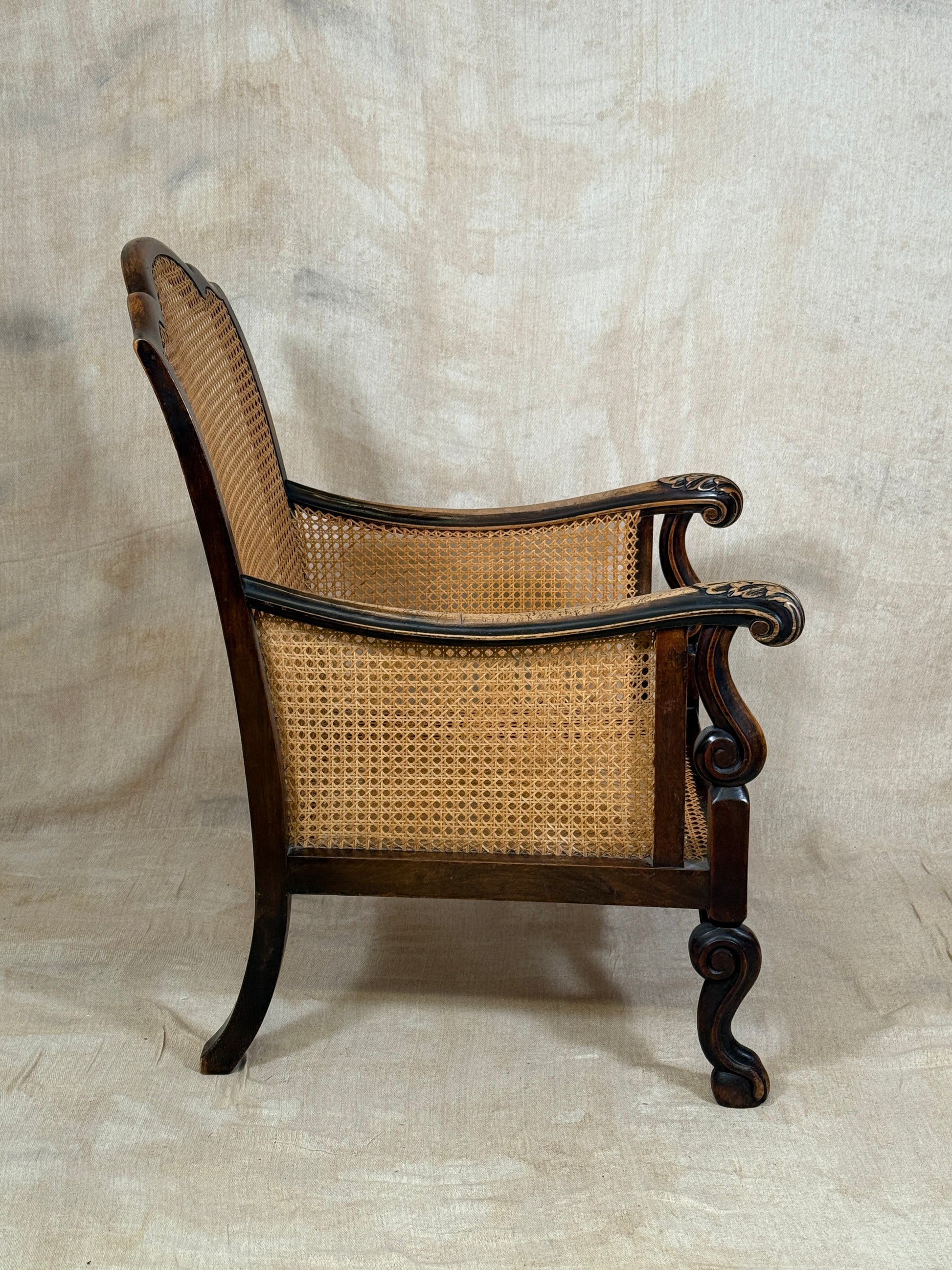 Antique Bergère style cane armchair and matching footstool with dark carved wooden frames and woven cane panels.