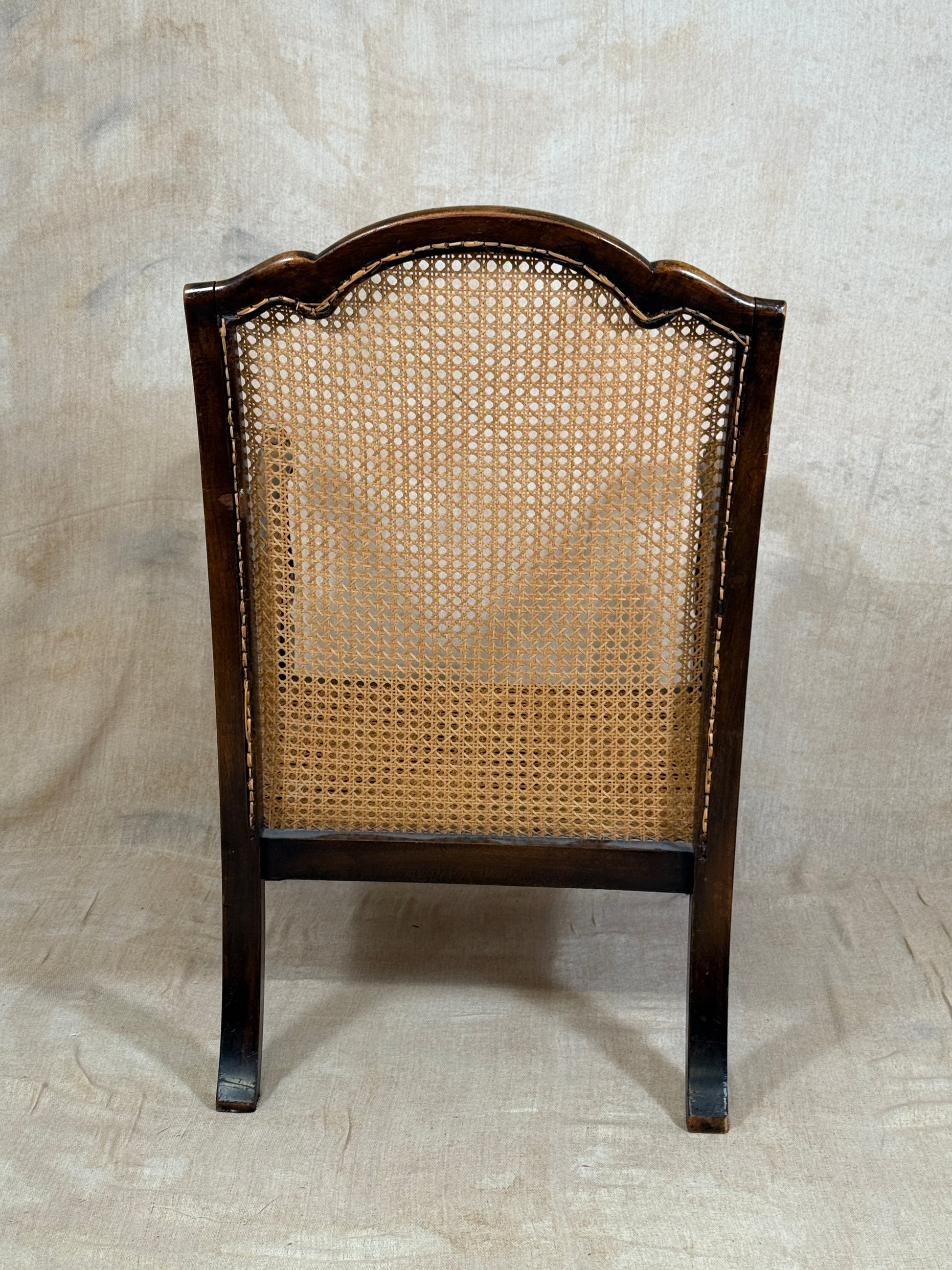 Antique Bergère style cane armchair and matching footstool with dark carved wooden frames and woven cane panels.