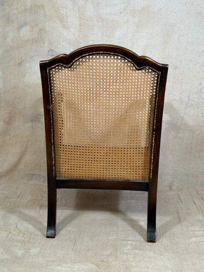 Antique Bergère style cane armchair and matching footstool with dark carved wooden frames and woven cane panels.