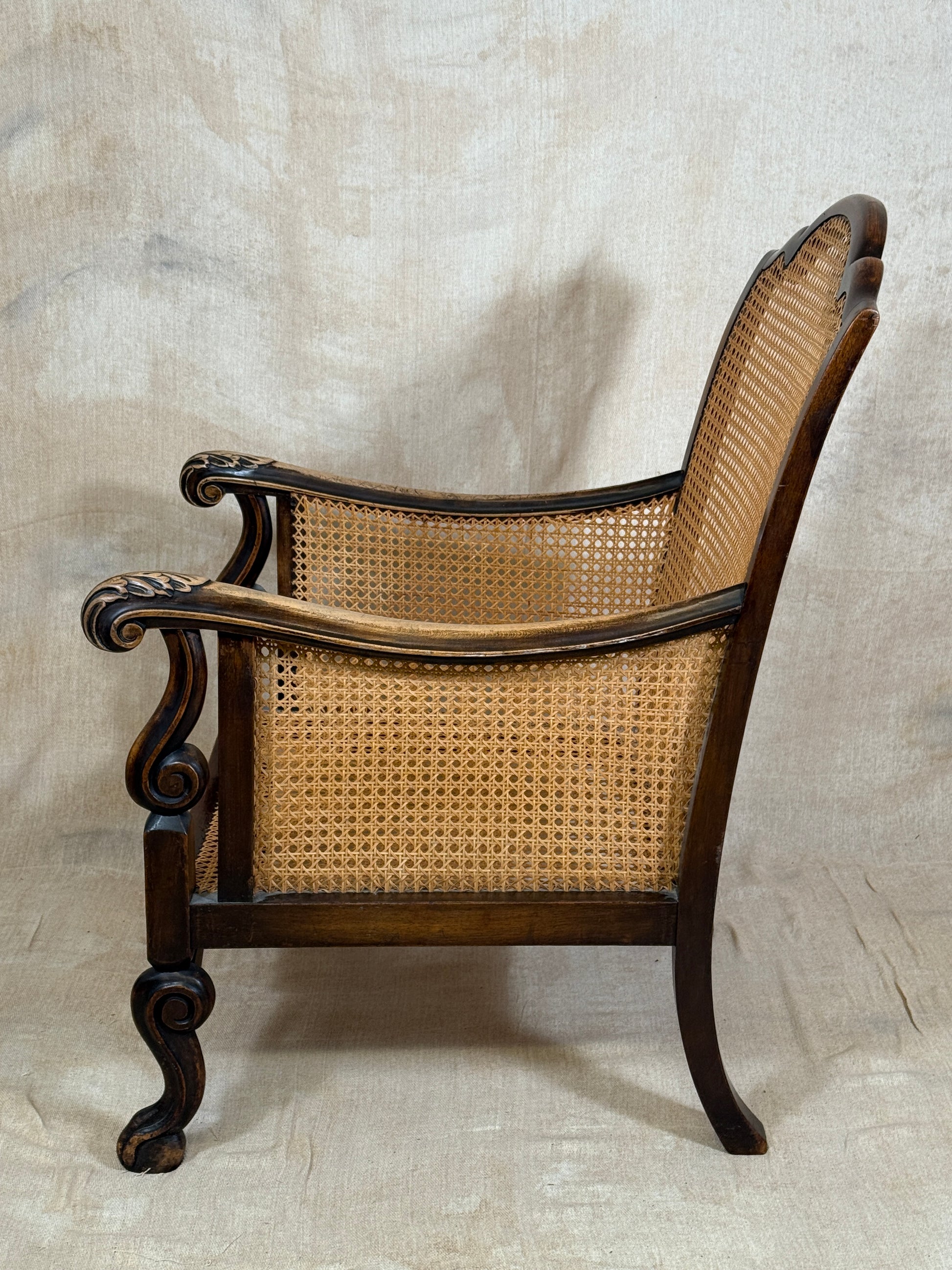 Antique Bergère style cane armchair and matching footstool with dark carved wooden frames and woven cane panels.