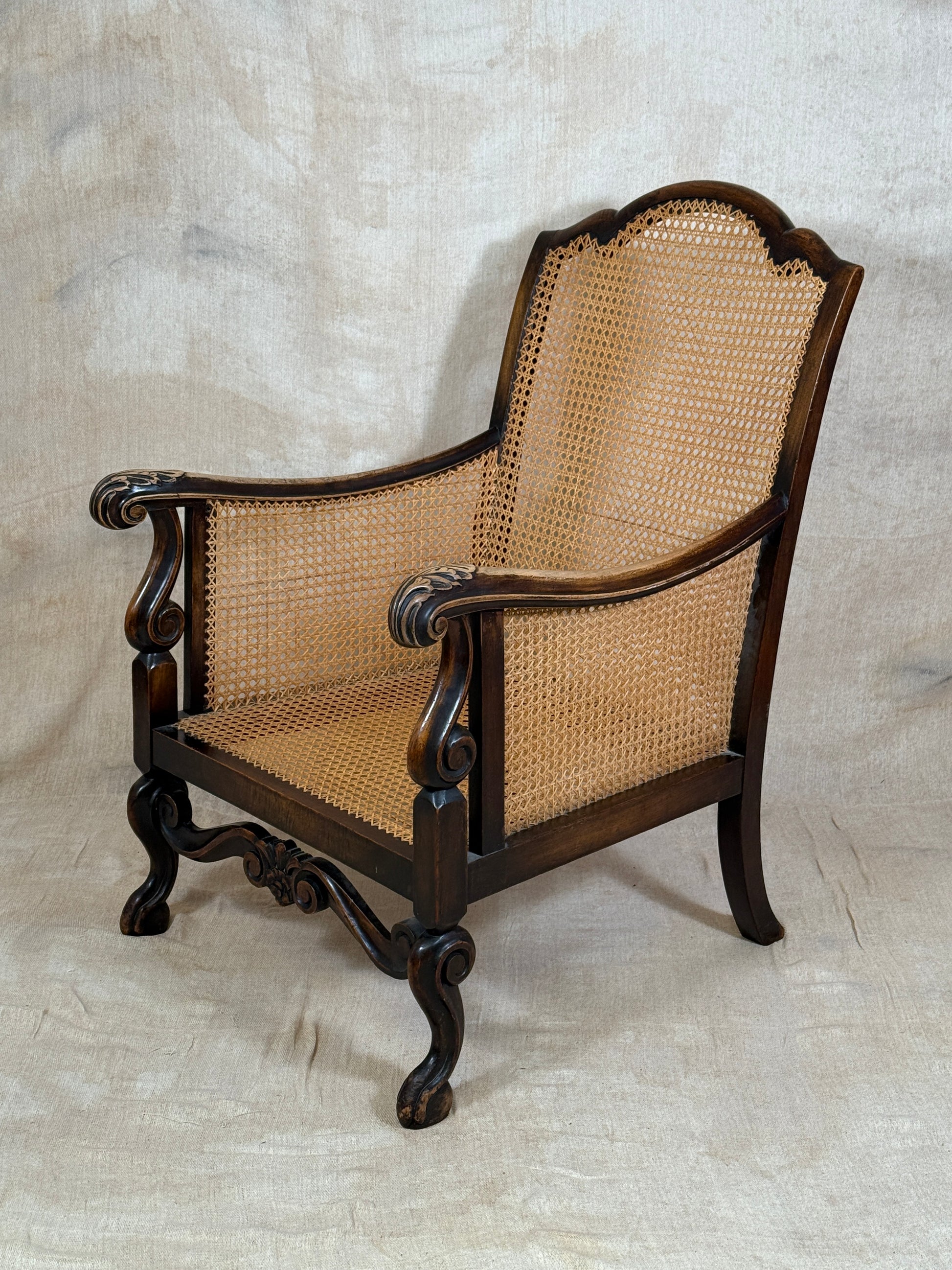 Antique Bergère style cane armchair and matching footstool with dark carved wooden frames and woven cane panels.