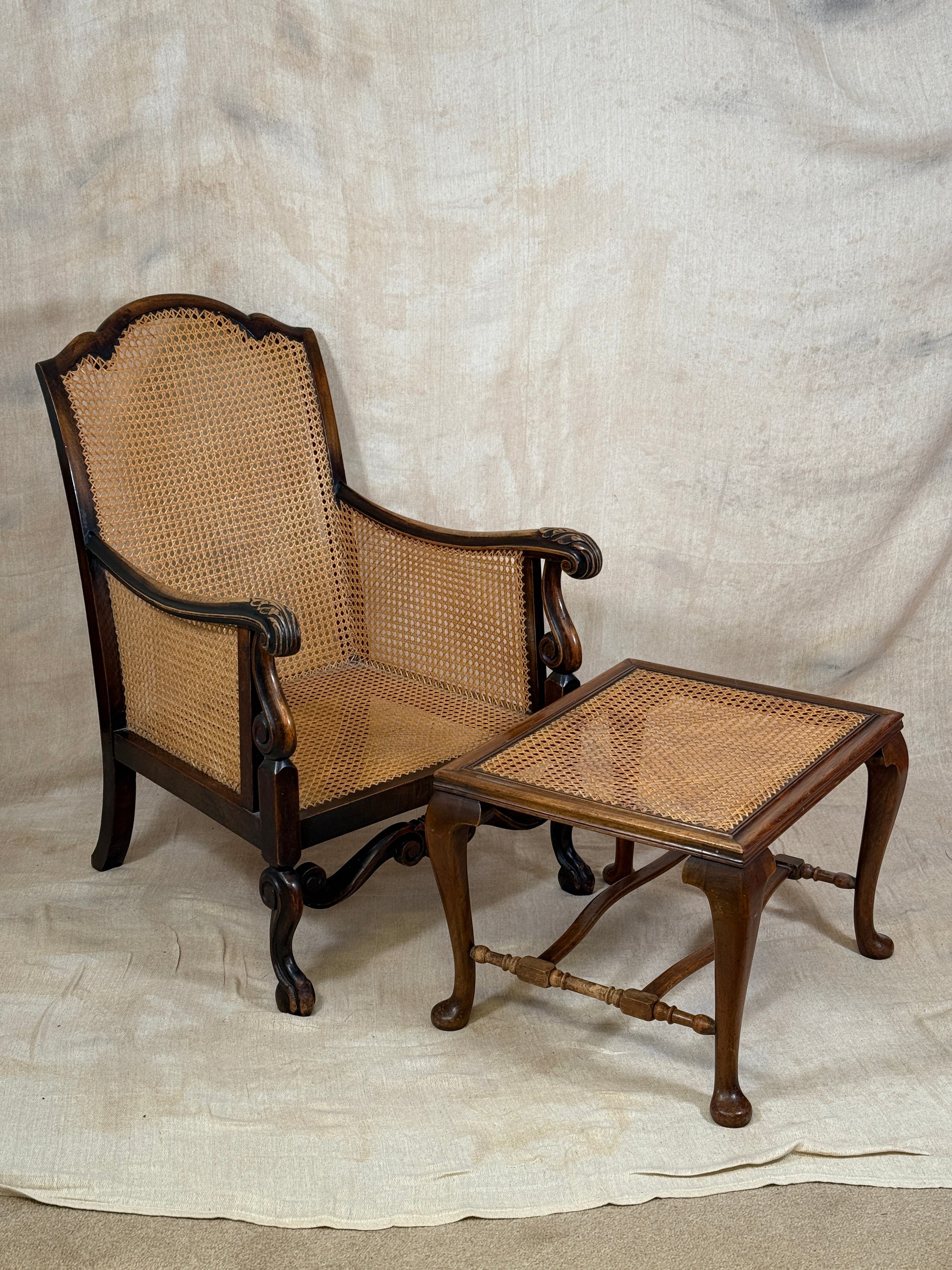 Antique Bergère style cane armchair and matching footstool with dark carved wooden frames and woven cane panels.