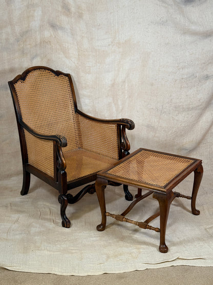Antique Bergère style cane armchair and matching footstool with dark carved wooden frames and woven cane panels.