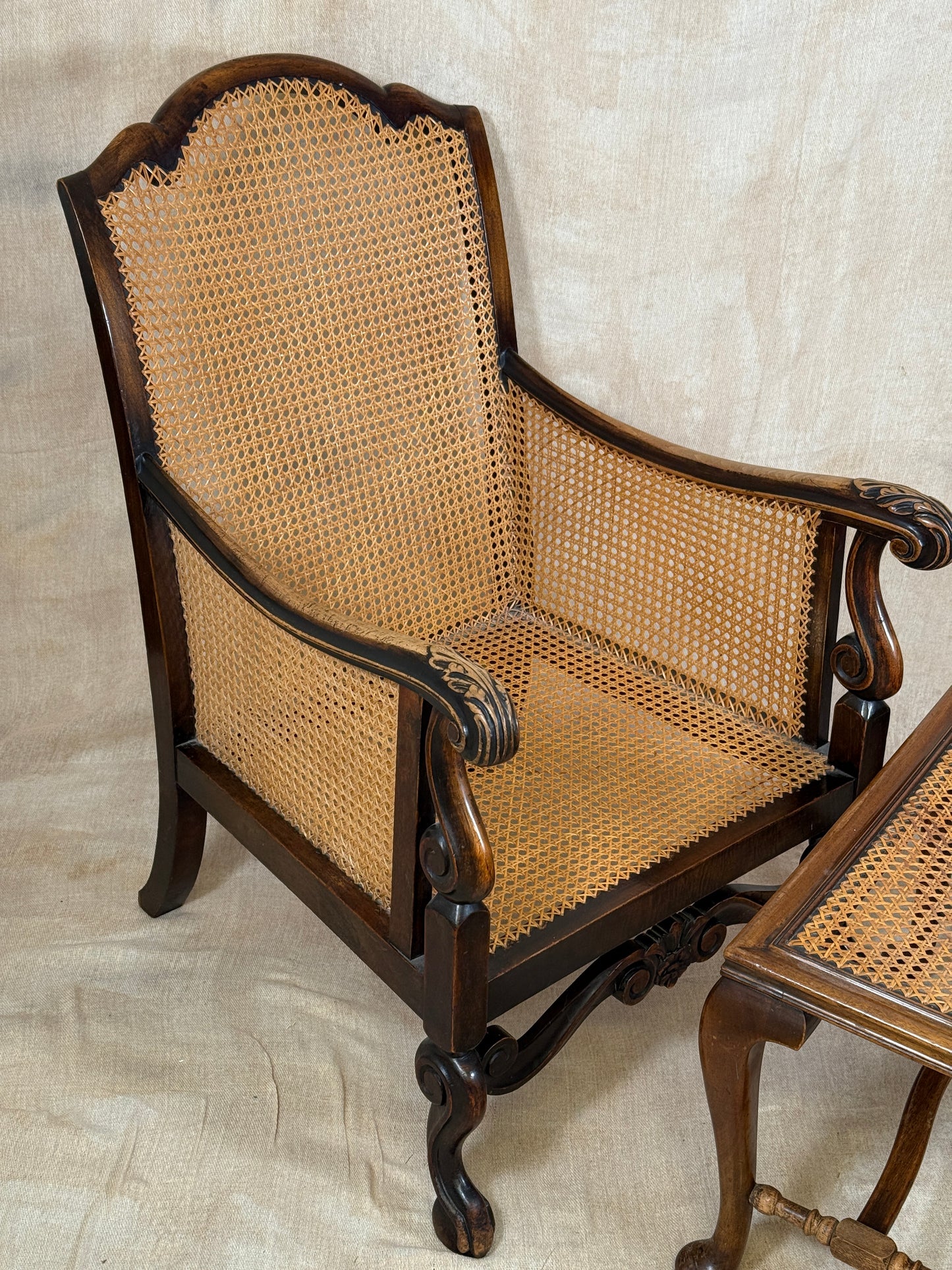 Antique Bergère style cane armchair and matching footstool with dark carved wooden frames and woven cane panels.