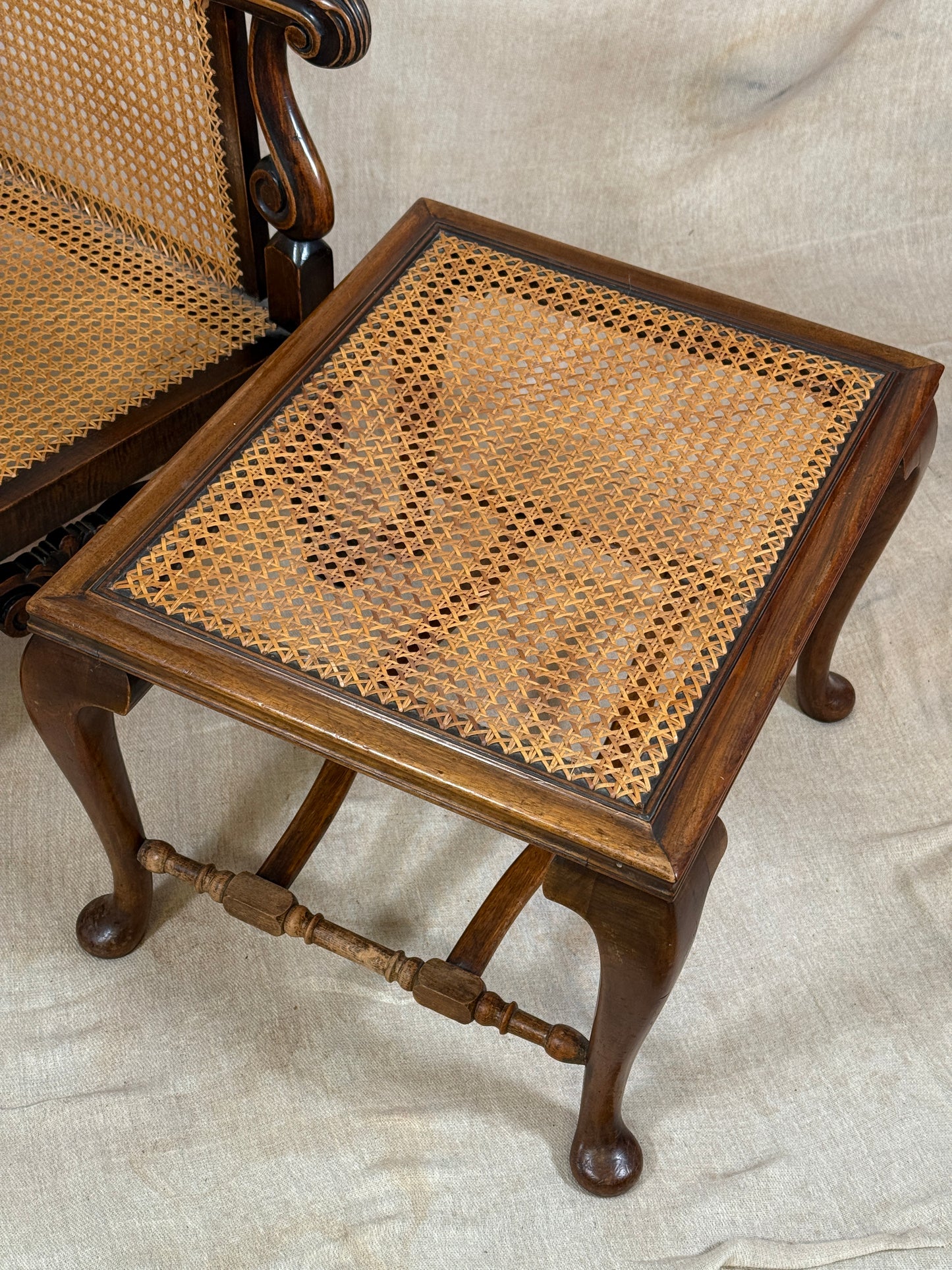 Antique Bergère style cane armchair and matching footstool with dark carved wooden frames and woven cane panels.
