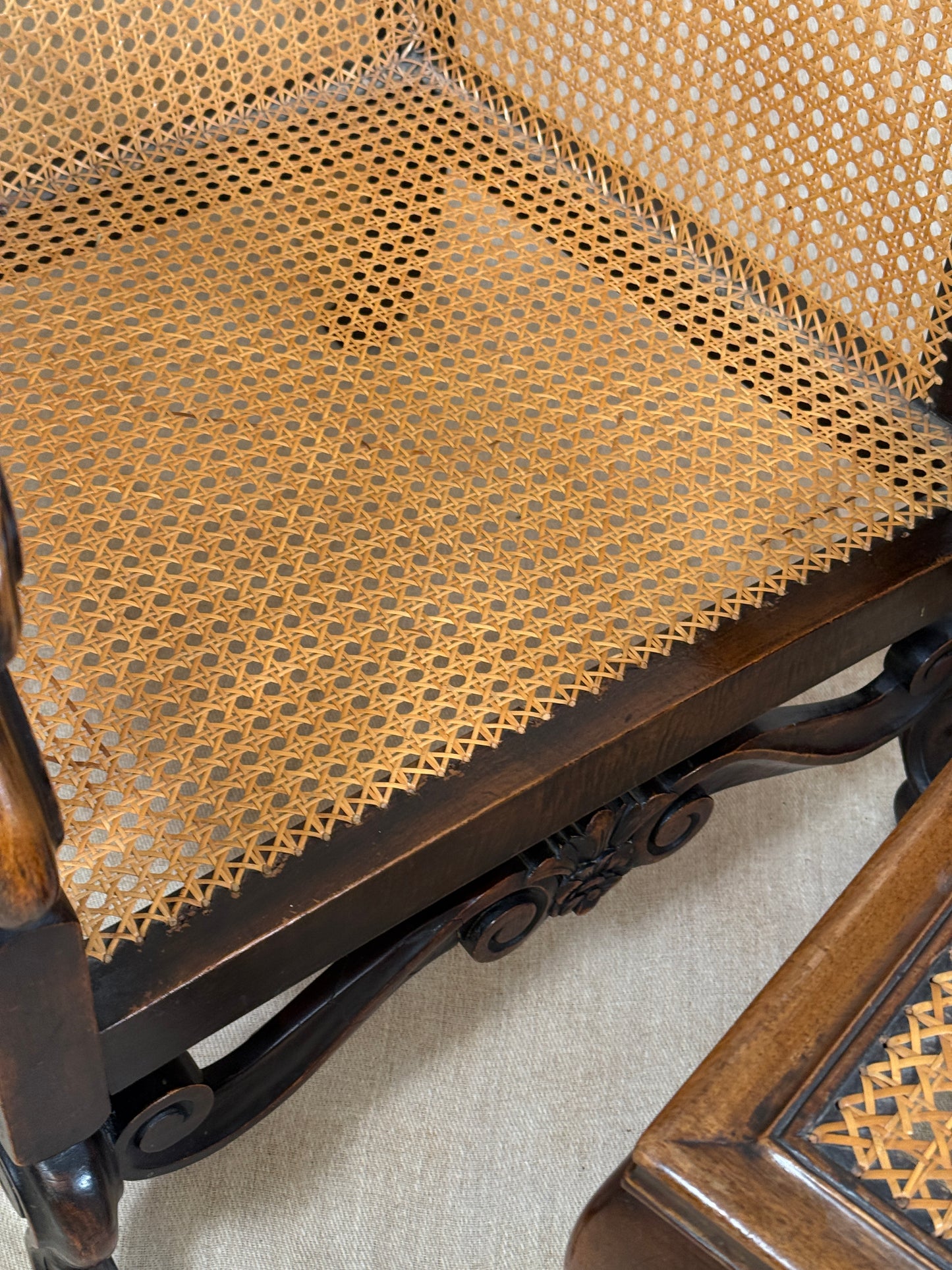 Antique Bergère style cane armchair and matching footstool with dark carved wooden frames and woven cane panels.