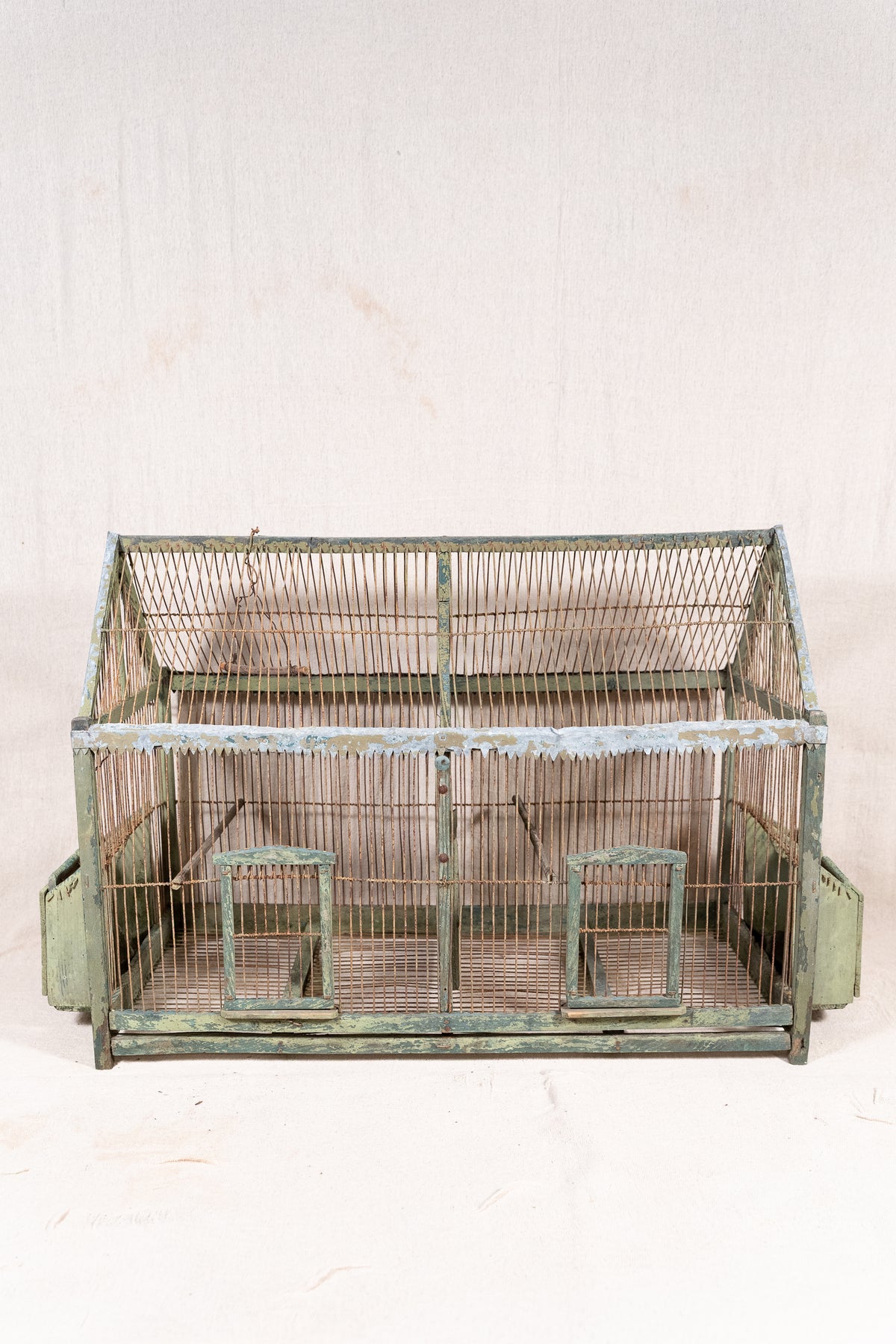 Vintage wooden birdcage with weathered green paint, decorative metal ridge detail, wire mesh panels and feeding troughs on both sides.