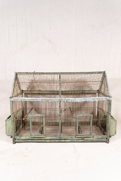 Vintage wooden birdcage with weathered green paint, decorative metal ridge detail, wire mesh panels and feeding troughs on both sides.