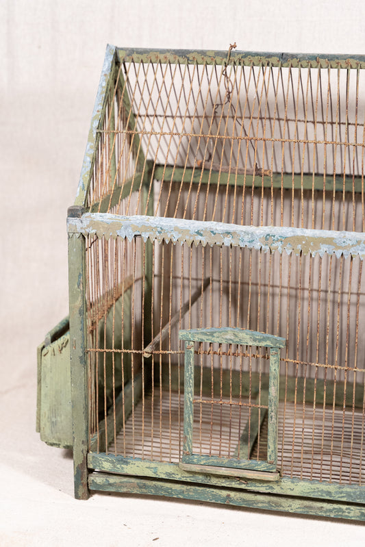 Vintage wooden birdcage with weathered green paint, decorative metal ridge detail, wire mesh panels and feeding troughs on both sides.