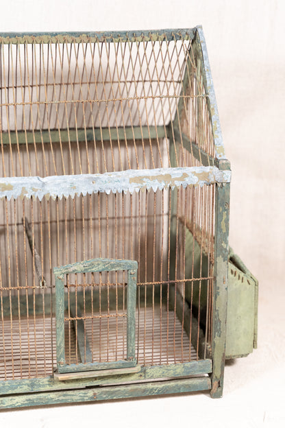 Vintage wooden birdcage with weathered green paint, decorative metal ridge detail, wire mesh panels and feeding troughs on both sides.