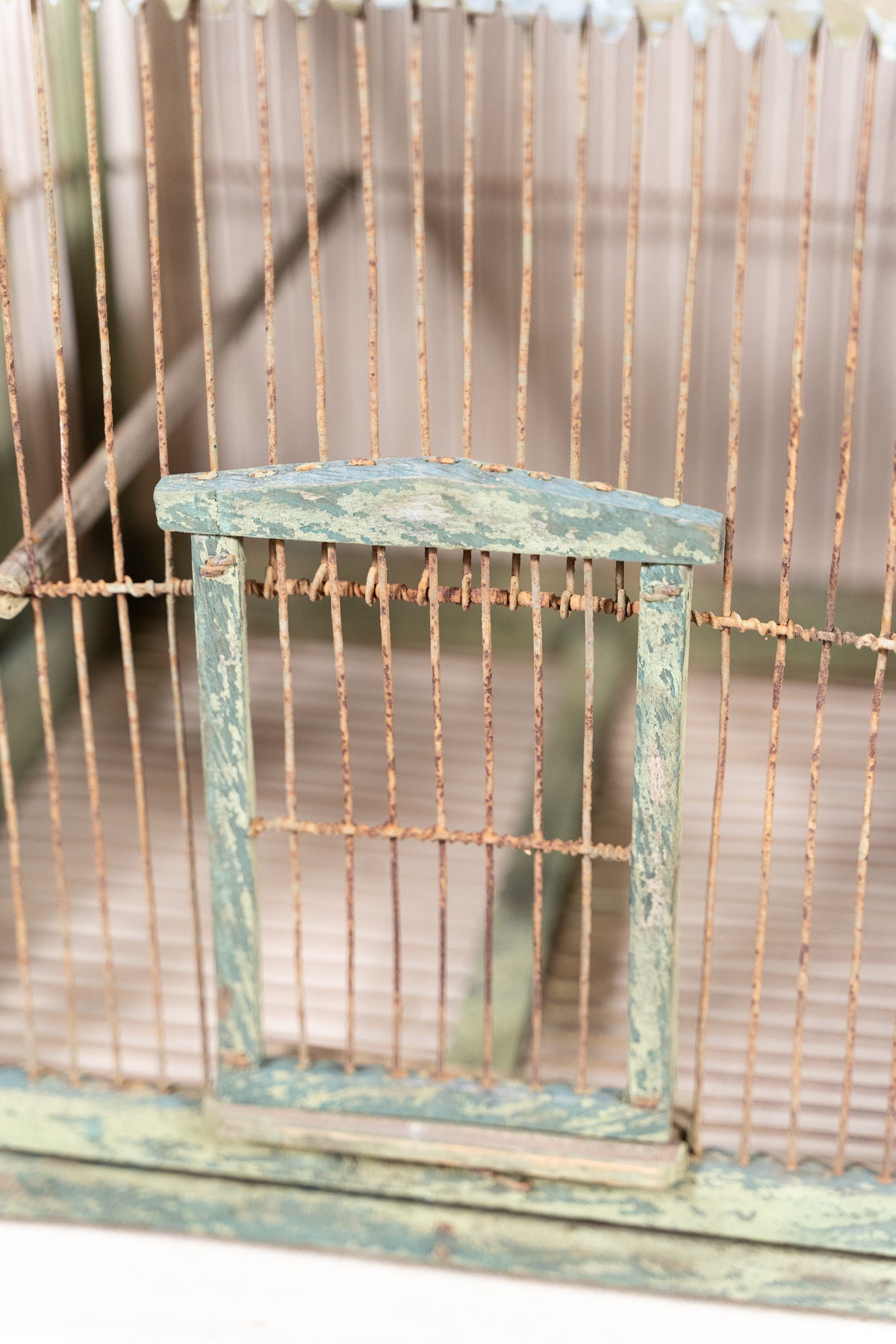 Vintage wooden birdcage with weathered green paint, decorative metal ridge detail, wire mesh panels and feeding troughs on both sides.
