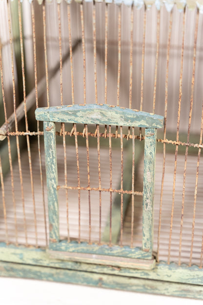 Vintage wooden birdcage with weathered green paint, decorative metal ridge detail, wire mesh panels and feeding troughs on both sides.